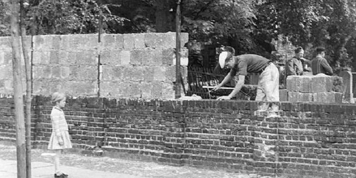 Здание стены. Девушка наблюдает за каменщиком из Восточной Германии, работающим на границе. - август 1961 г.
